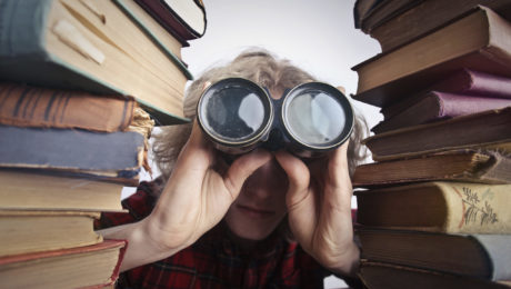 Canva - Anonymous person with binoculars looking through stacked books
